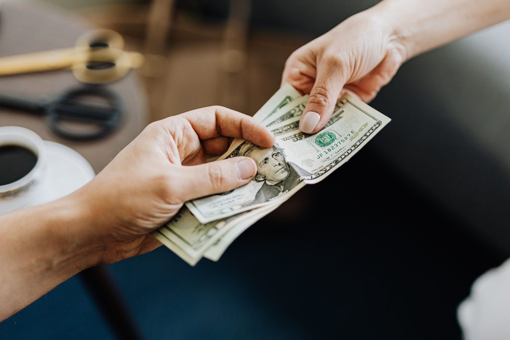 Hands exchanging cash, illustrating out-of-pocket costs and expenses for mental health insurance.