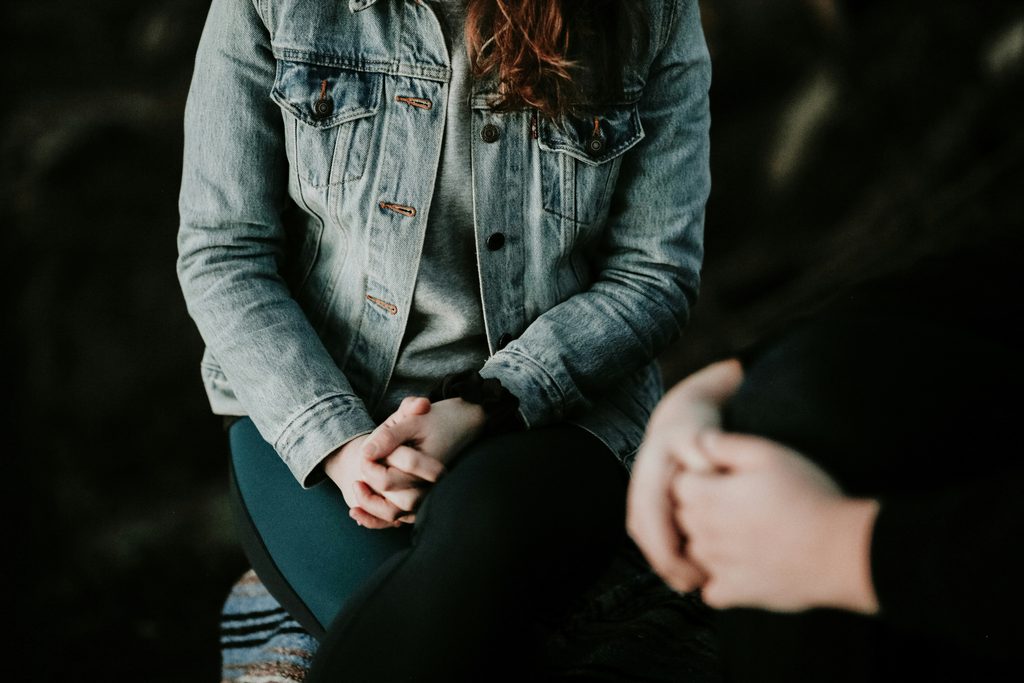 A teenager sitting with their back to the camera wearing a denim jacket, looking thoughtful or withdrawn on the topic of How to Help a Teen Struggling With Mental Health.