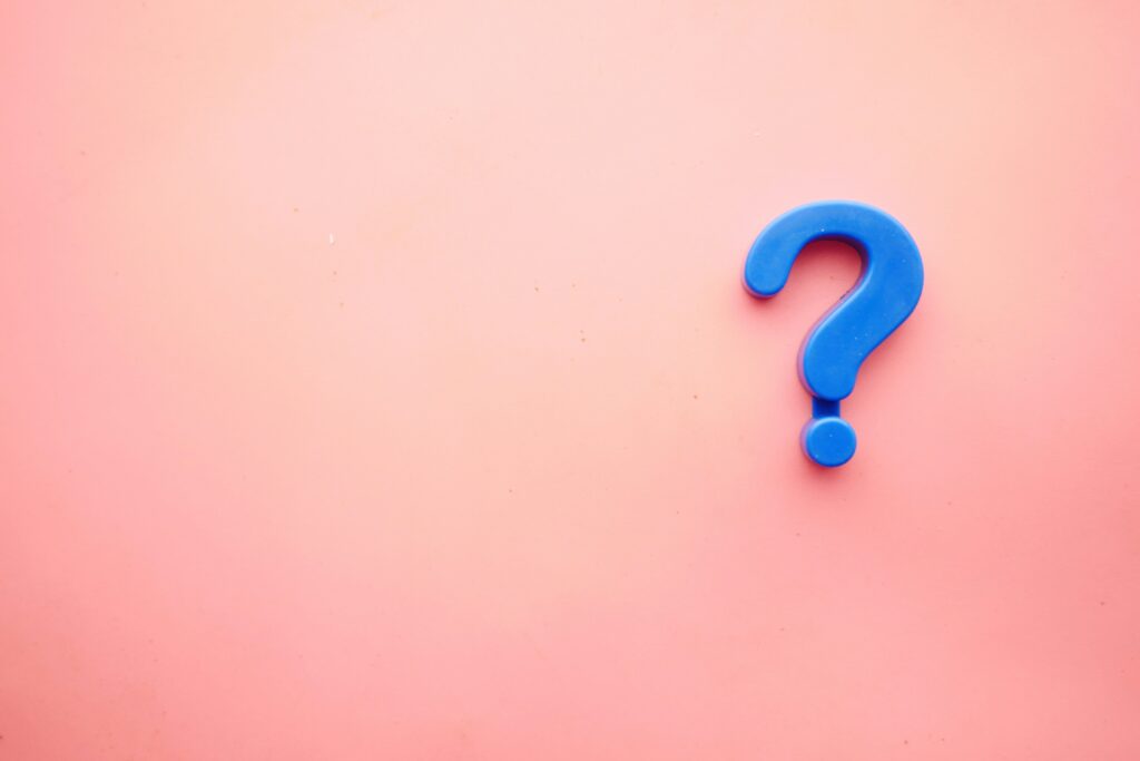 A large light-blue 3D question mark resting on a soft pink surface.